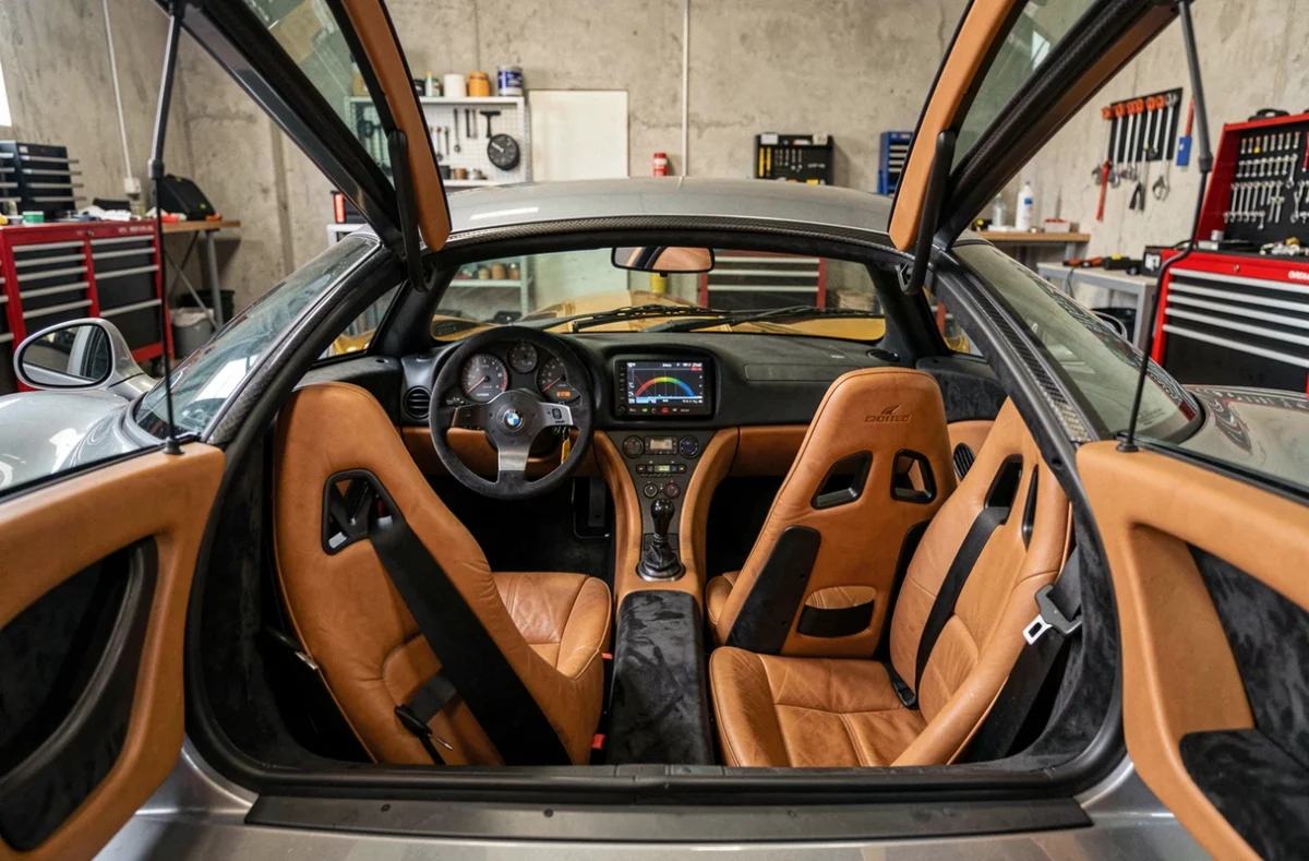 Intérieur de la McLaren F1 montrant le siège central emblématique, les sièges passagers latéraux en cuir beige et Alcantara, et le compartiment moteur doré visible